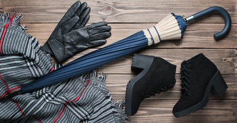 Suede black boots, gloves, scarf, umbrella on wood background. Top view