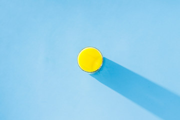 A glass of orange juice on a blue background. Concept of vitamins, tropic, summertime, drink of thirst. Minimalism. Natural light. Flat lay, top view.