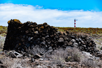 Im Hintergrund vor einer Hausruine ist der Leuchtturm Faro de Rasca zu sehen