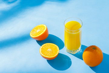 A glass of orange juice and oranges on a blue background. Concept of vitamins, tropic, summertime....
