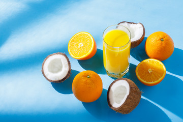 A glass of orange juice, oranges and coconuts on a blue background. Concept of vitamins, tropic, summertime, drink of thirst. Natural light. Flat lay, top view.