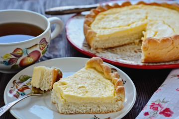Freshly baked homemade shortbread dough pie with cottage cheese filling and one cutted piece of cake on a plate next to spoon with little piece of cake in it