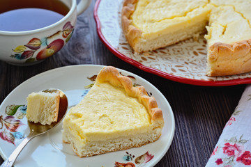 Freshly baked homemade shortbread dough pie with cottage cheese filling and one cutted piece of cake on a plate next to spoon with little piece of cake in it, closeup