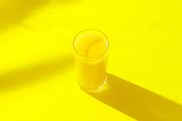 A glass of orange juice on a yellow background. Concept of vitamins, tropic, summertime, drink of thirst. Minimalism. Natural light. Flat lay, top view.