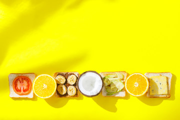 Sandwiches with banana, tomato, avocado, blue cheese and fresh fruits, orange and coconut on a yellow background. Concept of a healthy breakfast, vitamins, diet. Flat lay, Top view.