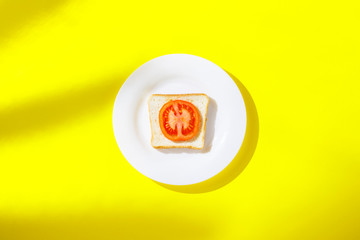 Sandwich with tomato on a white plate on a yellow background. Healthy breakfast concept, vitamins, diet, weight loss. Flat lay, Top view