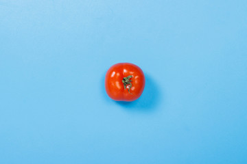 Tomato on a blue background. Concept of vitamins, summertime, breakfast. Flat lay, top view.