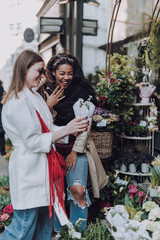 Two cheerful young women visiting outdoor flower shop