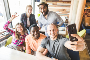 Fototapeta premium Group of young cheerful friends are sitting in a cafe, eating, drinking drinks. Friends take selfies and take pictures.