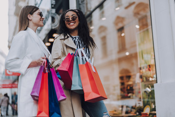 Two beautiful cheerful women with shopping bags standing on the street