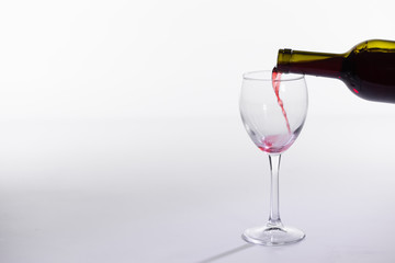 Red wine pouring into glass from bottle on white background with copy space