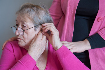 elderly retired with hearing impairment received hearing aid of latest modification in center of social protection. nurse helps to try hearing aid on. Help for seniors and people with disabilities