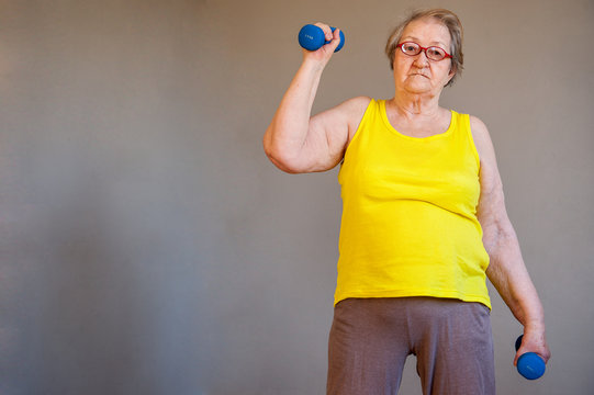 elderly woman in yellow T-shirt and sportswear does gymnastics with dumbbells. Little boys grandchildren do exercises with their grandmother.