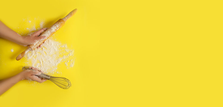 Female hands holding kitchen tools, sieve, rolling pin, bowl, sieve, brush, whisk,  cooking over yellow background. Food frame, bake concept with copy space.Flat lay top view banner