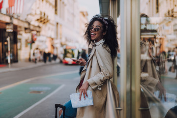 Beautiful afro american girl in trench coat using cellphone on the street