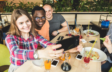 Group of young cheerful friends are sitting in a cafe, eating, drinking drinks. Friends take selfies and take pictures.