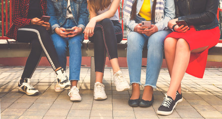 Millennials style. Young people in trendy denim outfits standing with smartphones, reading messages, posts in social networks.