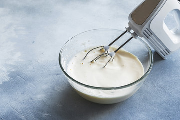 Whipped cream with a mixer in a glass bowl