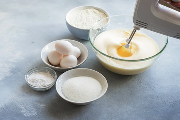 Fototapeta na wymiar Mixer whipping eggs in a glass bowl and ingredients to create a cake 