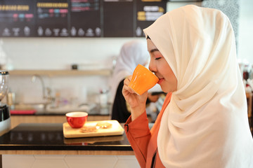 muslim customer drinking coffee at counter with young muslim barista girl working blurred background