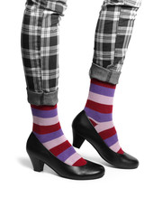 Women's legs in checkered trousers, colorful striped socks and black high heel shoes.
