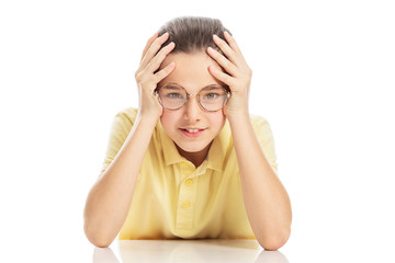 Teen girl with glasses sitting at the table, laughing and holding her head. Isolated on a white background.