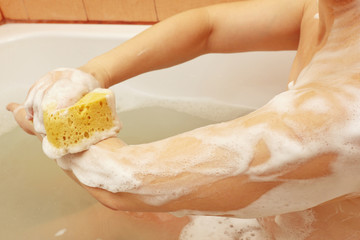 Fototapeta premium Beautiful young woman lathering sponge hand in the bathroom close up
