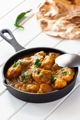 Closeup traditional Indian butter chicken curry and lemon served with chapati bread in iron-cast. Wooden background
