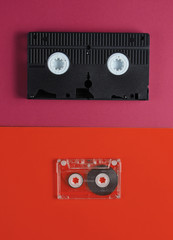 Pop culture media 80s. Audiotape, videotape on orange red background. Top view