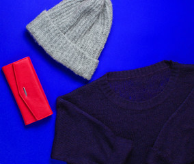 Women's fashion items on blue background. Sweater, warm hat, red purse. Top view