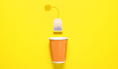 Cardboard tea cup and teabag on yellow background. Top view. Minimalism