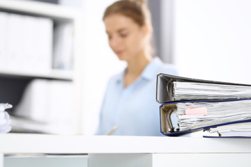 Binders with papers are waiting to be processed by business woman or bookkeeper back in blur....