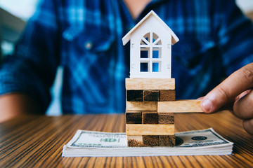 Hand holding a piece of wood block with model white house on dollar banknote. Insurance and...