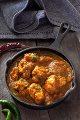 Close up traditional Indian butter chicken curry and lemon served with chapati bread in iron-cast. Wooden background.