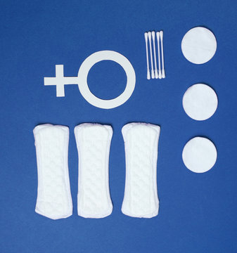 Products for feminine hygiene, self-care and health, female gender symbol on blue background. Ear sticks, pads. Top view