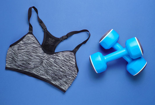 Fitness concept. Sports bra, dumbbells on blue background. Top view, minimalism