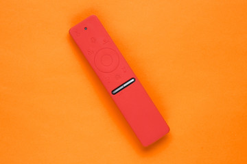 Modern TV remote in silicone case on orange background. Top view, minimalism