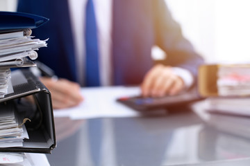 Binders with papers waiting to be processed with businessman or bookkeeper back in blur. Accounting planning budget. Audit, insurance  and business concept