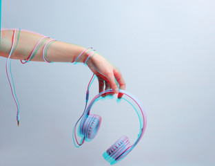 Hand wrapped cable holds blue headphones on gray background. Glitch effect