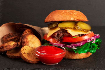 Closeup of delicious fresh homemade burger with lettuce, cheese, onions and tomatoes on dark background