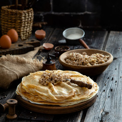 Homemade stack of crepes on wooden plate stand on rustic table with plate of ground fried beef
