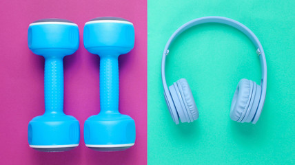Blue headphones, plastic dumbbells on mint purple background. Sports with music. Flat lay. Top view.