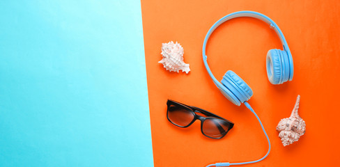 Summer rest concept. Headphones, sunglasses, shells on orange-blue background. Beach music. Top view. Copy space