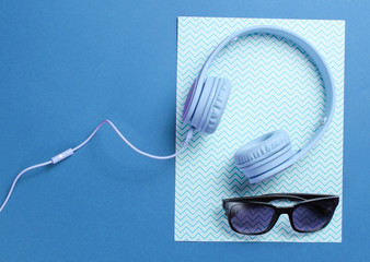 Blue headphones with cable, sunglasses on blue creative background. Minimalism. Top view