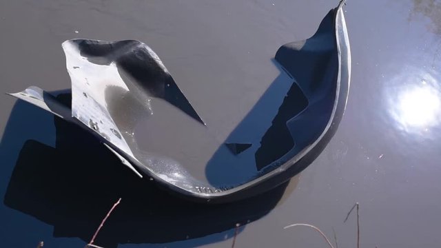 The torn off wing of an old black car floats in a puddle on a bad road in bright daylight  The inner part of the wing of the car in a puddle of water in the absence of asp 