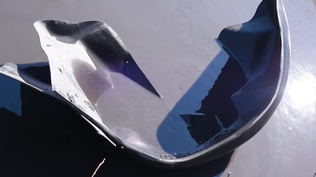 The torn off wing of an old black car floats in a puddle on a bad road in bright daylight  The inner part of the wing of the car in a puddle of water in the absence of asp 