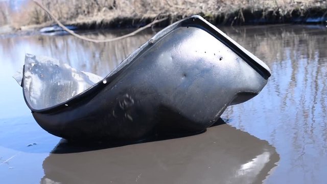 The torn off wing of an old black car floats in a puddle on a bad road in bright daylight  The inner part of the wing of the car in a puddle of water in the absence of asp 