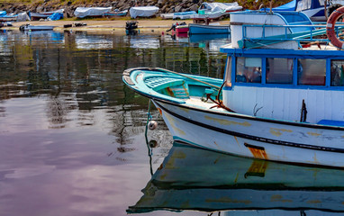 Fototapeta na wymiar Colorful fishing boats in a harbour on a clear sunny day with blue skies reflected in the calm water.