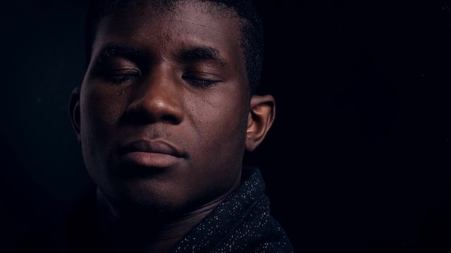 sad lonely black african man in the darkness, staring at camera