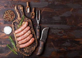 Raw beef and pork sausage on old chopping board with vintage knife and fork on dark wooden...